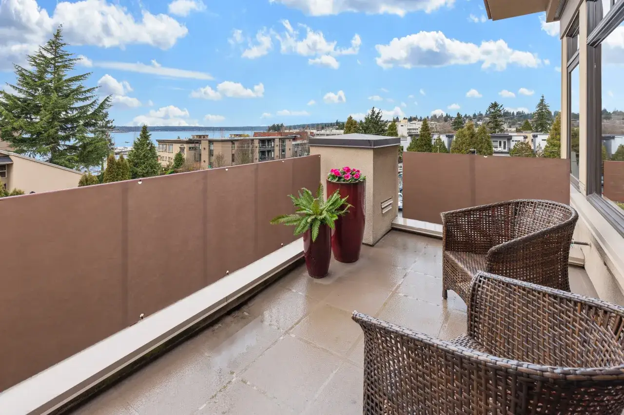 Zrelaksowany balkon w bloku z widokiem na wodę. Wygodne fotele i donice z kwiatami tworzą przytulną przestrzeń.