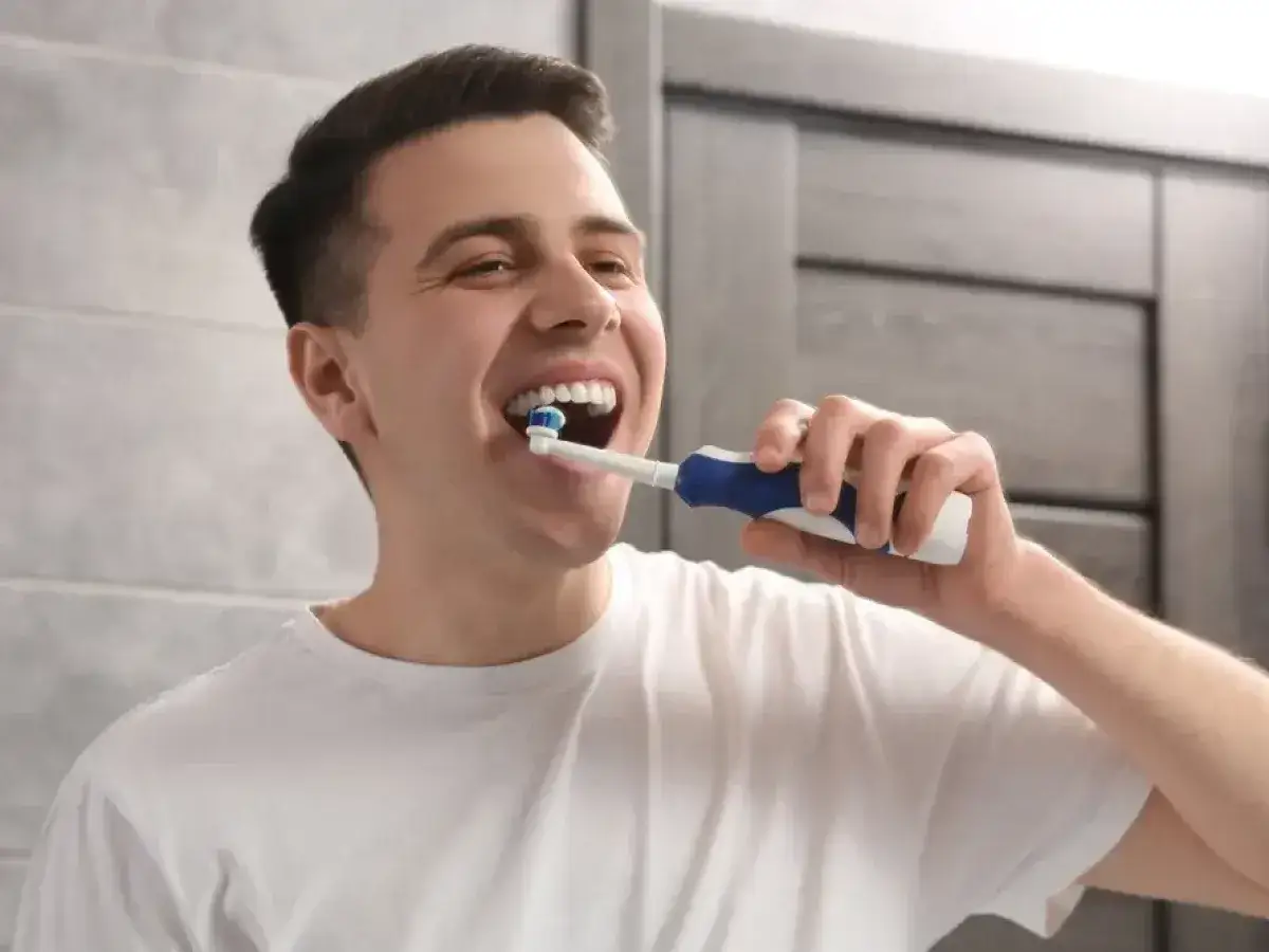 Uśmiechnięty mężczyzna pokazuje, jak myć zęby szczoteczką elektryczną. Białe zęby i czysta łazienka.