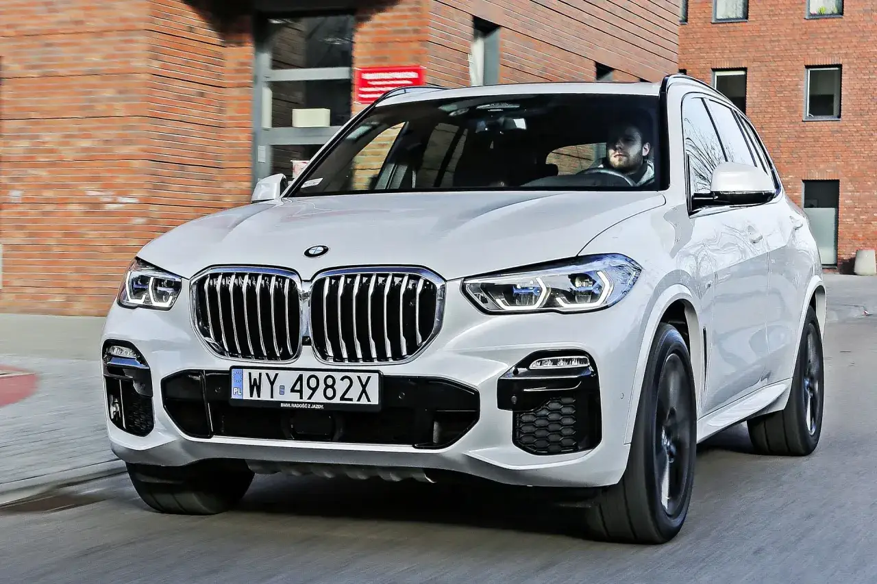 Białe BMW X5 w ruchu miejskim. Kierowca za kierownicą. Poznaj szczegółowe bmw x5 dane techniczne.