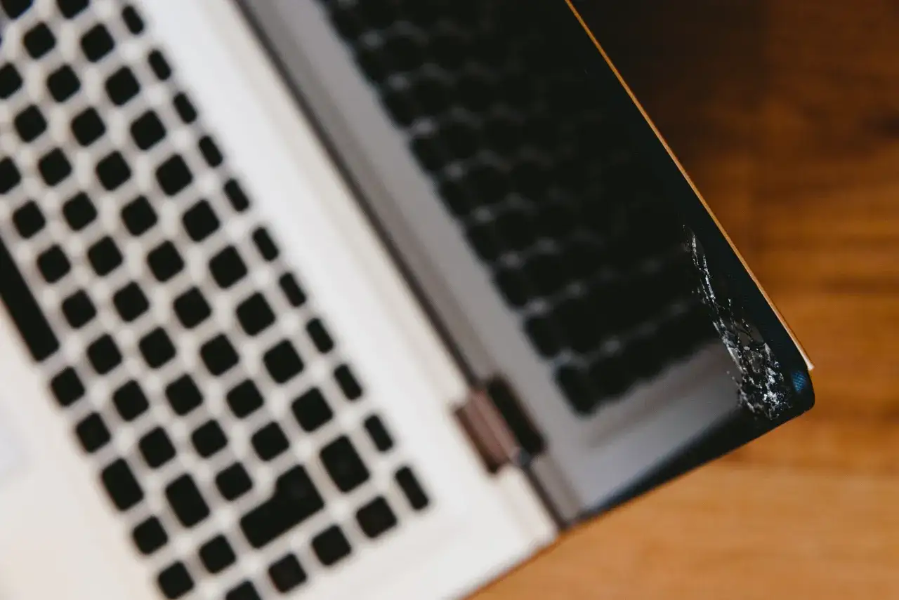 Uszkodzona bateria w laptopie objawy: wybrzuszenie obudowy i pęknięcia. Widoczna klawiatura i fragment obudowy.