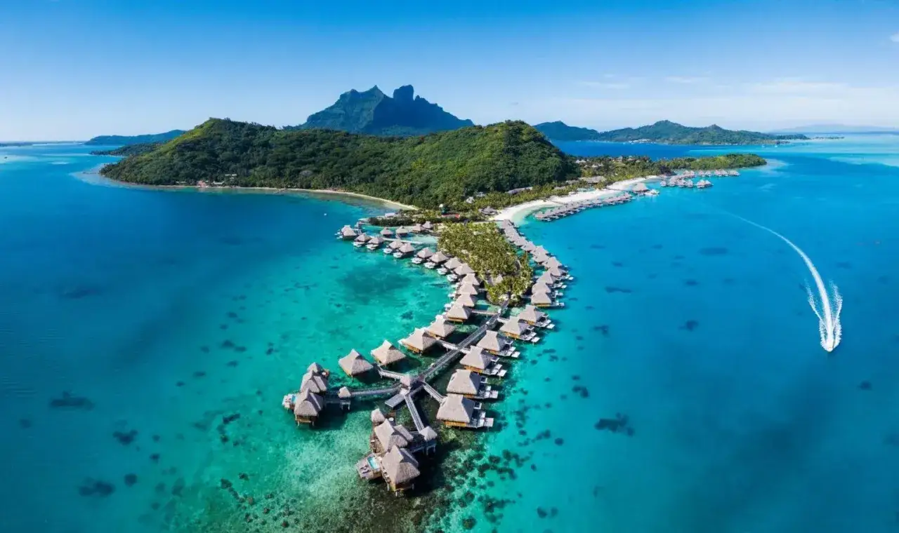 Rajskie widoki na Bora-Bora, gdzie leży ten luksusowy kurort z domkami na wodzie i górami w tle.