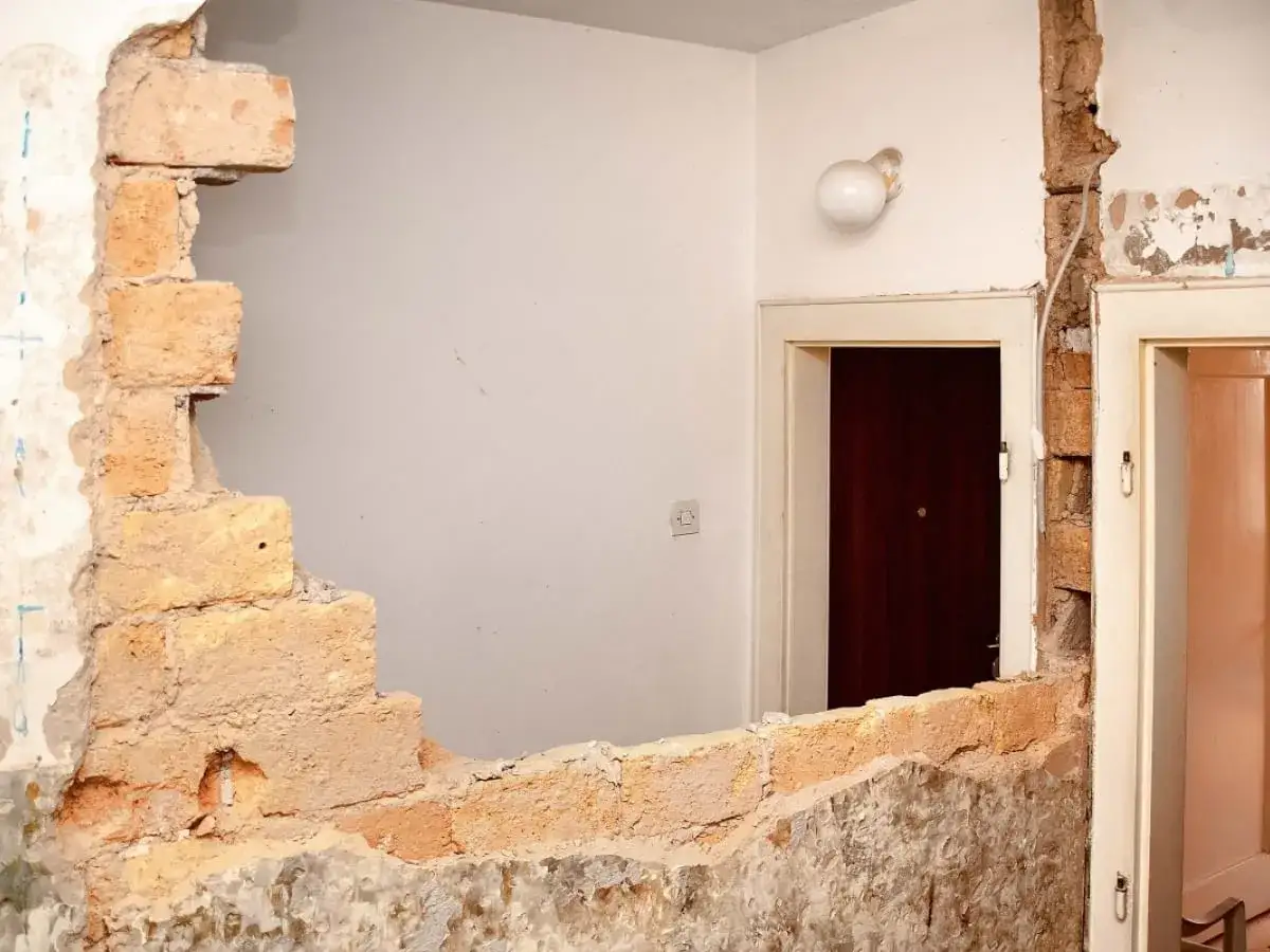 Remont w toku. Zastanawiasz się, ile kosztuje wyburzenie ściany? Widok na fragment zburzonej ceglanej ściany, drzwi i białe ściany.