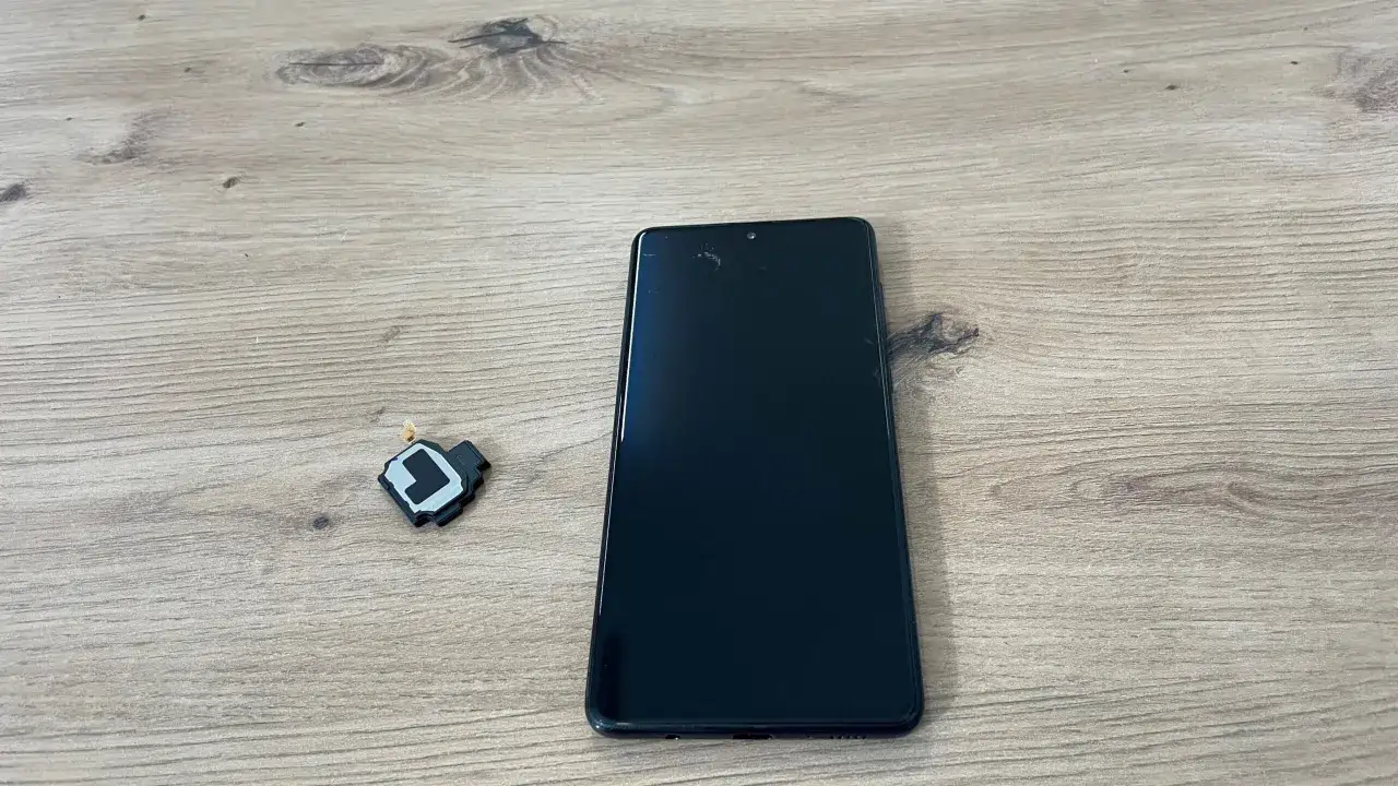 Uszkodzony głośnik telefonu leży obok czarnego smartfona. To może być powód, dlaczego głośnik w telefonie trzeszczy.