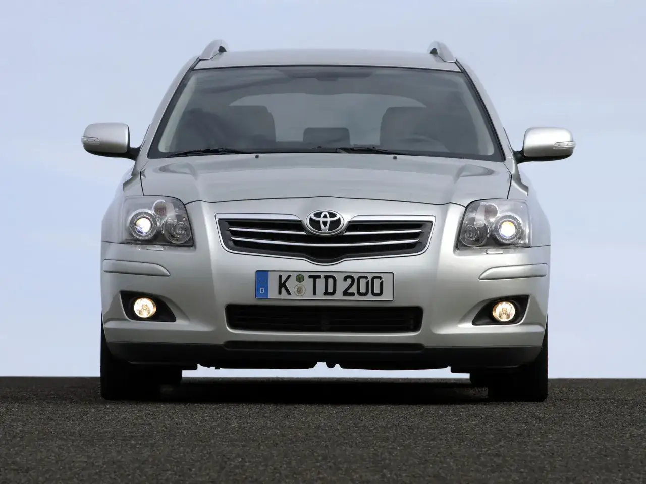 Srebrny Toyota Avensis z włączonymi światłami mijania i przeciwmgielnymi, gotowy do podróży.