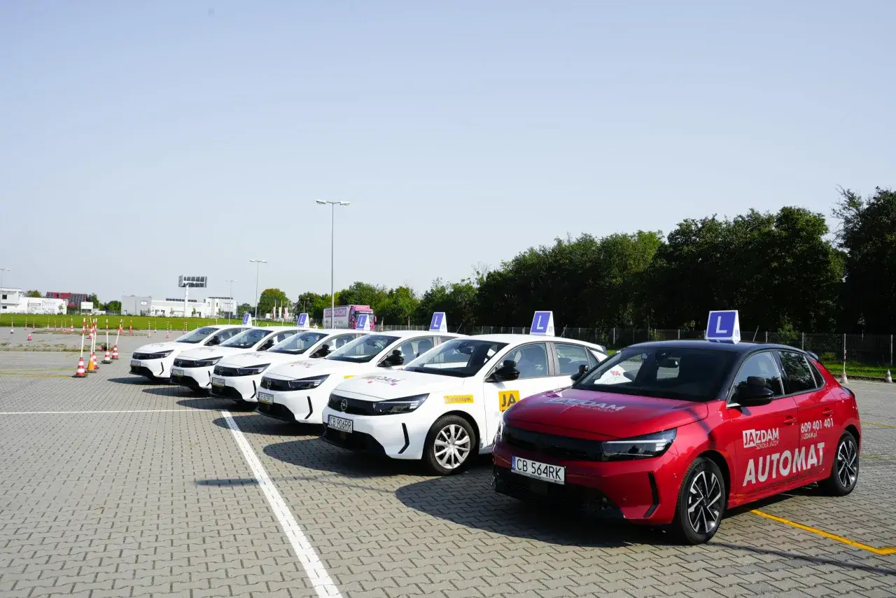 Rząd białych i czerwony samochód nauki jazdy na placu manewrowym. Zastanawiasz się, ile kosztuje prawo jazdy w Polsce?