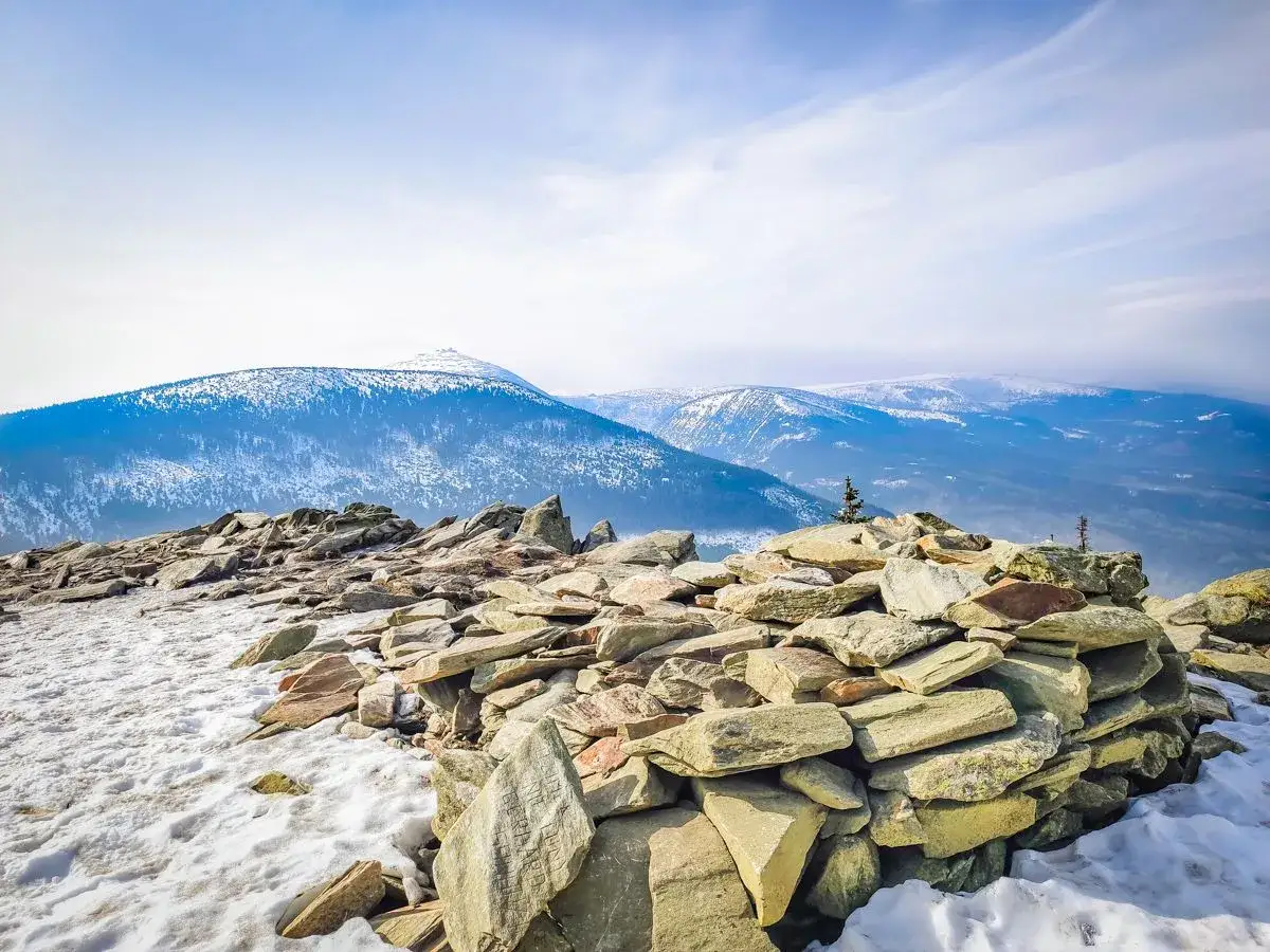 Kamienny kopiec na skalistym szczycie, z widokiem na ośnieżone g&oacute;ry. To miejsce, gdzie kończy się droga, a zaczyna przygoda na przełęczy okraj.