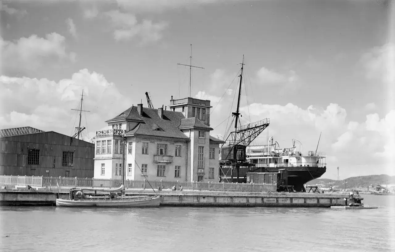 Portowe budynki i statki, widok z lat międzywojennych. Dźwig portowy obsługuje statek.