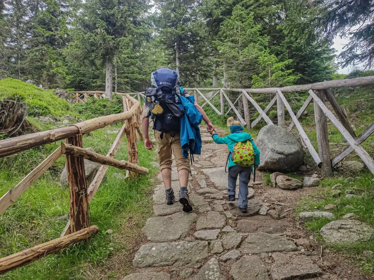 Dzieci i dorośli wędrują kamienistym szlakiem w Karkonoszach, otoczeni lasem. To piękna pielgrzymka do Karpacza.