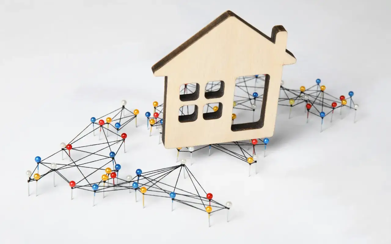 Drewniany domek na sieci kolorowych pinezek symbolizuje, kiedy najem prywatny staje się działalnością gospodarczą.