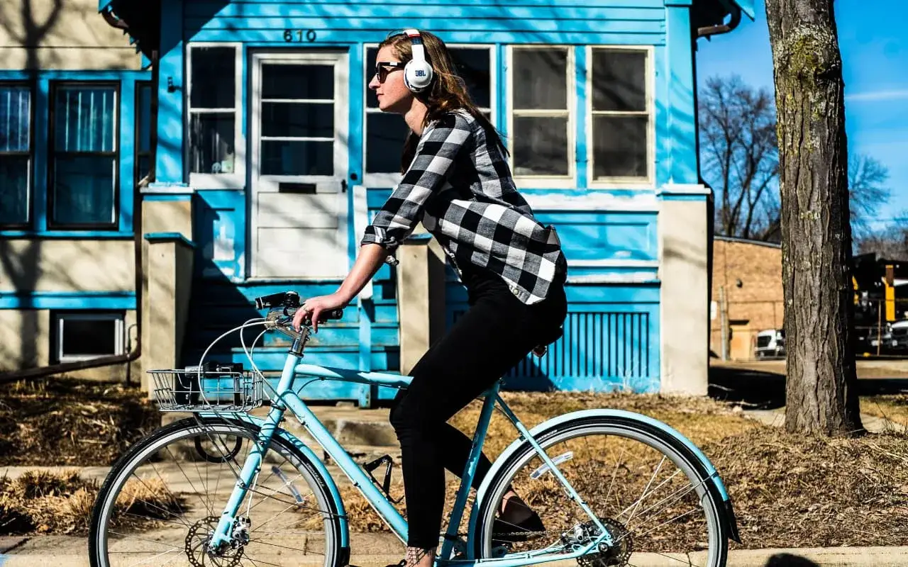 Dziewczyna w słuchawkach JBL na rowerze, zastanawia się jakie słuchawki na rower wybrać, by cieszyć się muzyką podczas jazdy.