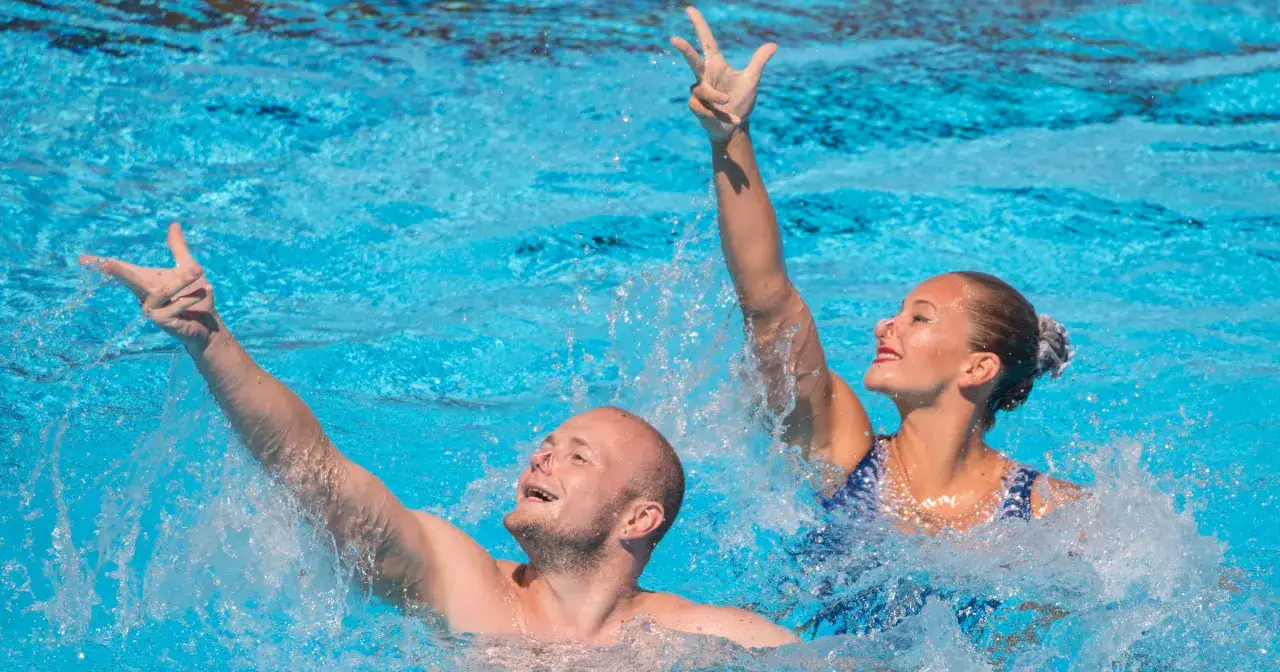 Para w basenie wykonuje efektowne ruchy podczas pływania synchronicznego, unosząc ręce w wodzie.
