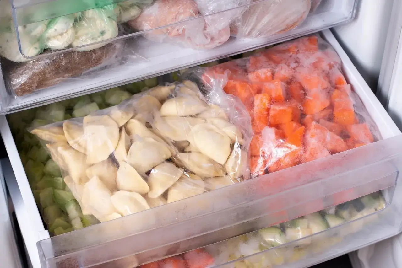 Zamrożone pierogi w woreczku, obok pokrojonej marchewki i cukinii. To świetny sposób, jak mrozić pierogi na później.