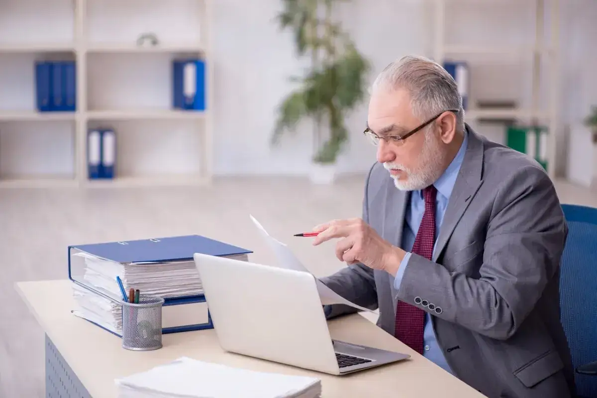 Starszy mężczyzna w garniturze analizuje dokumenty, zastanawiając się, kto nie płaci funduszu pracy.