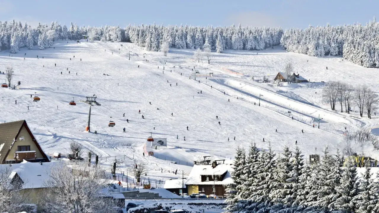 Zimowy dzień w Zieleńcu. Widać liczne trasy narciarskie, wyciągi i narciarzy szusujących po ośnieżonych stokach.