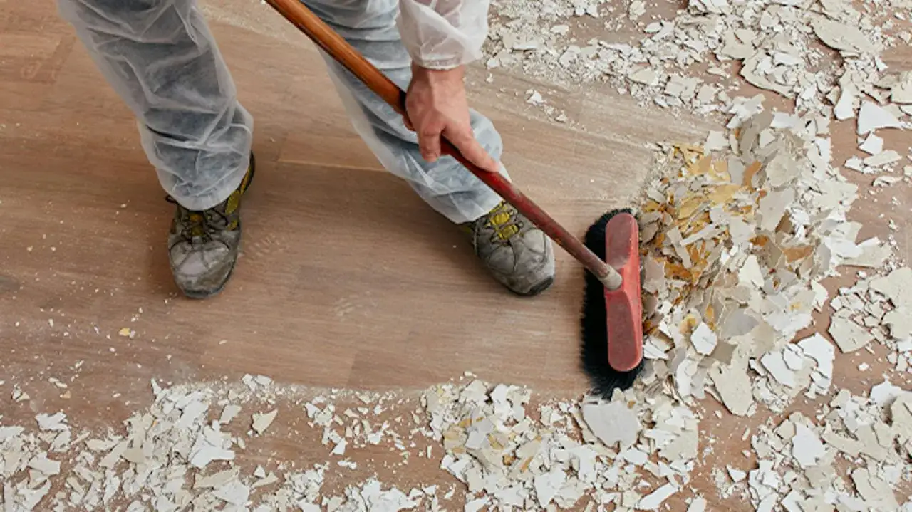 Osoba w kombinezonie sprząta gruz po tapetowaniu. Zastanawiasz się, gdzie wyrzucić tapetę? Zbieraj ją do worka i oddaj do punktu zbi&oacute;rki odpad&oacute;w budowlanych.