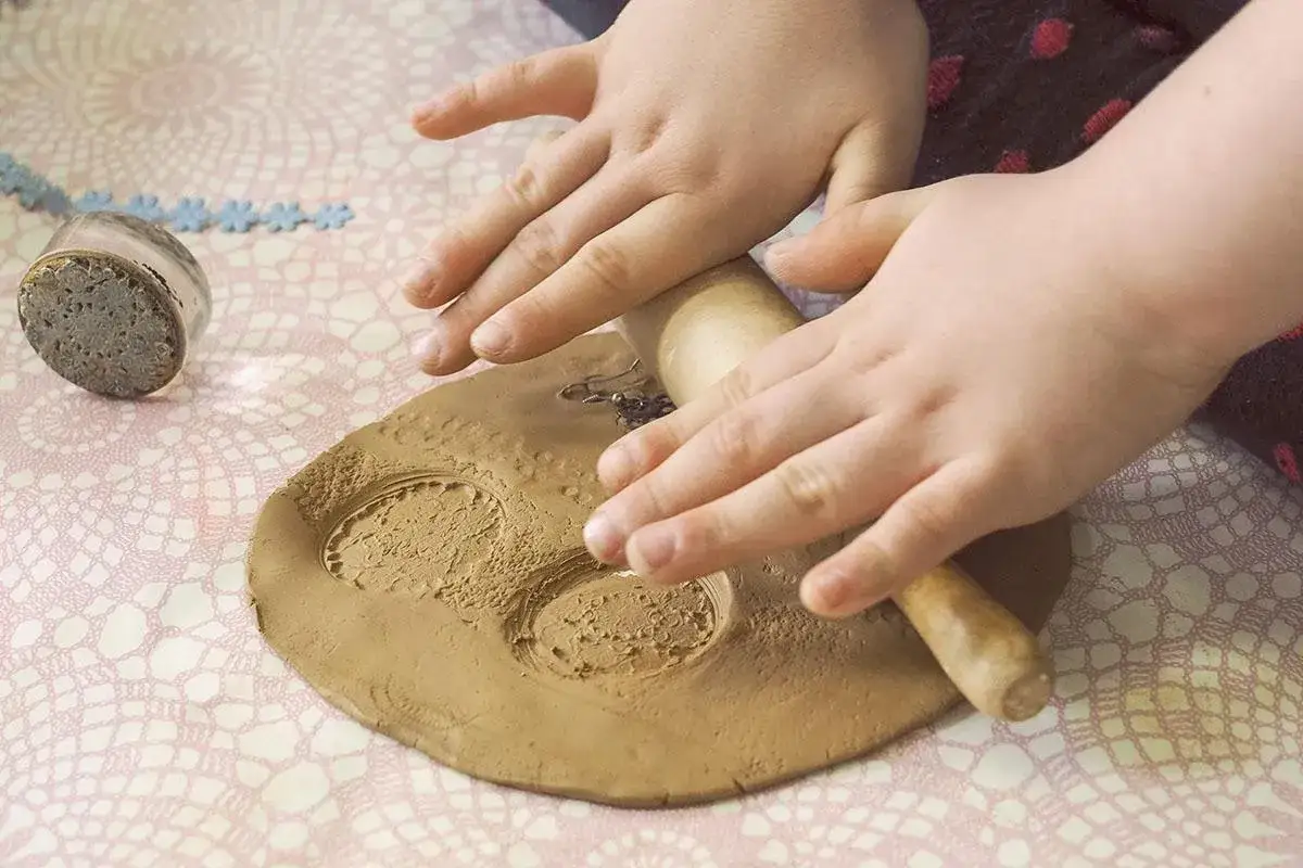Dziecko na warsztatach z garncarstwa wałkuje glinę, tworząc wzory.
