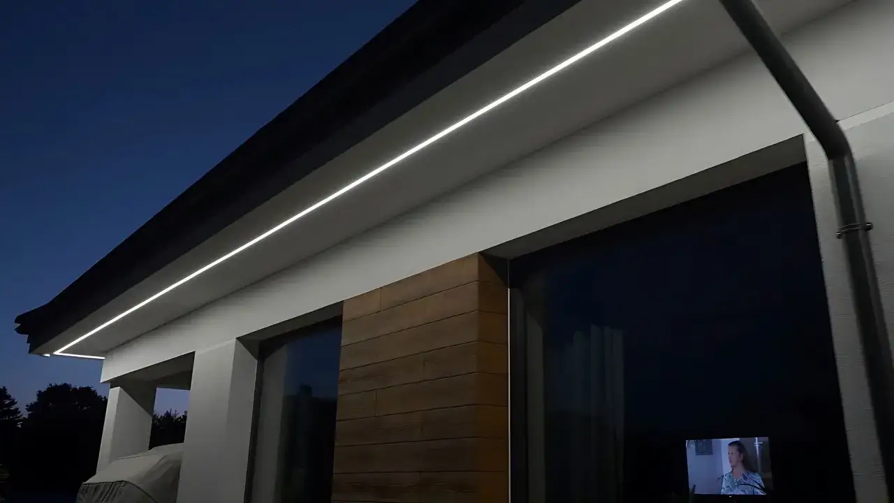 Nowoczesny montaż lamp na elewacji podkreśla architekturę domu. Białe linie światła biegną wzdłuż dachu, tworząc subtelny blask.