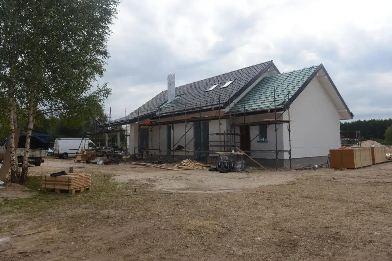 Budowa domu kanadyjskiego w toku. Widać rusztowania, materiały budowlane i częściowo wykończony dach.