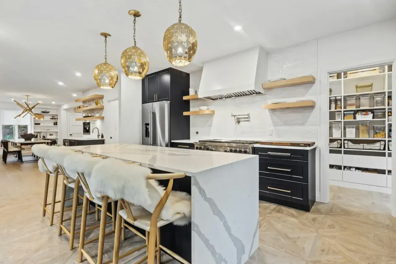 Elegante mueble cocina isla con encimera de cuarzo, taburetes de piel y lámparas doradas.