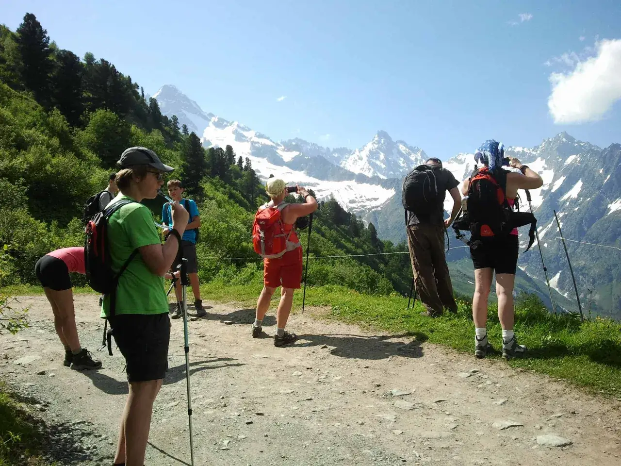 Grupa turystów w górach, każdy w wygodnym stroju, pokazuje, jak się ubrać w góry: krótkie spodenki, koszulki, plecaki i kije trekkingowe.