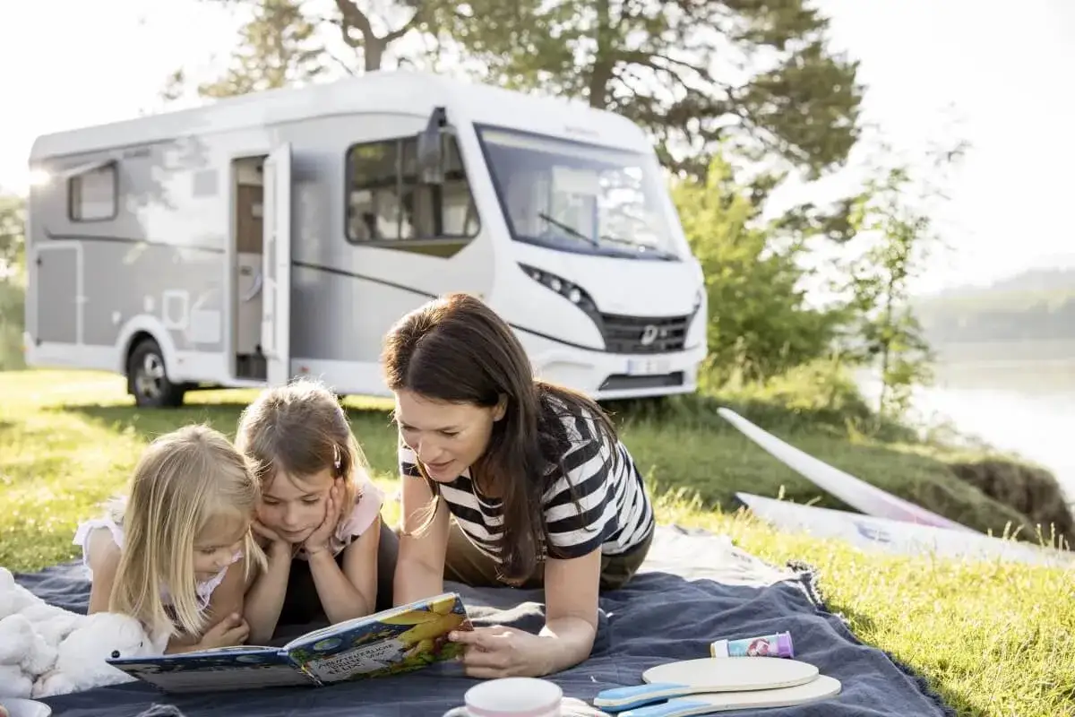 Rodzina czyta książkę przy kamperze. Zastanawiasz się, ile kosztuje kamper? To marzenie o wolności i przygodach.