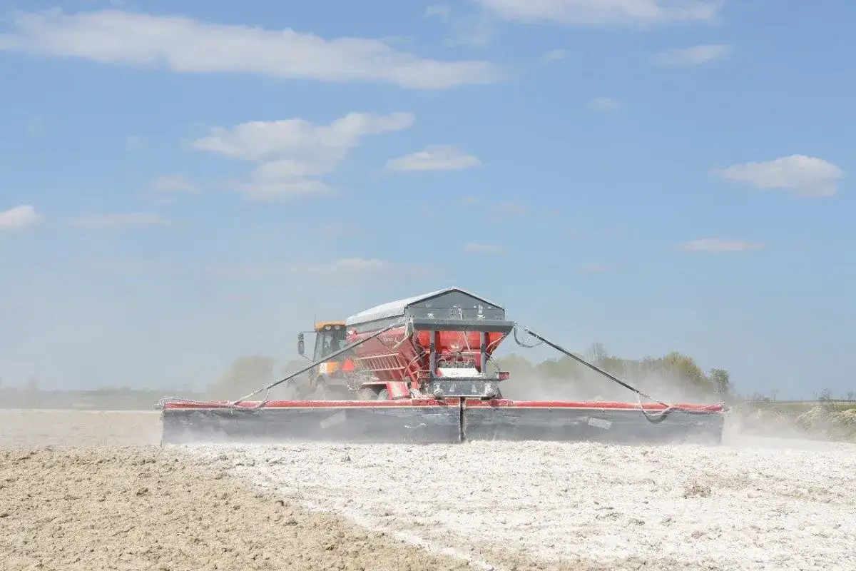 Traktor rozsypuje wapno do ziemi, poprawiając jej jakość.