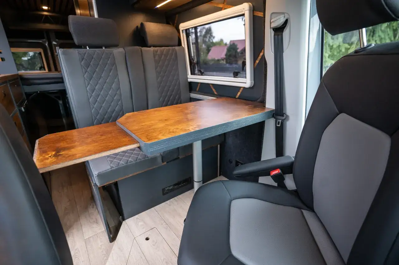 Wnętrze kampera: rozkładany stolik, wygodne siedzenia i okno z widokiem na domy.