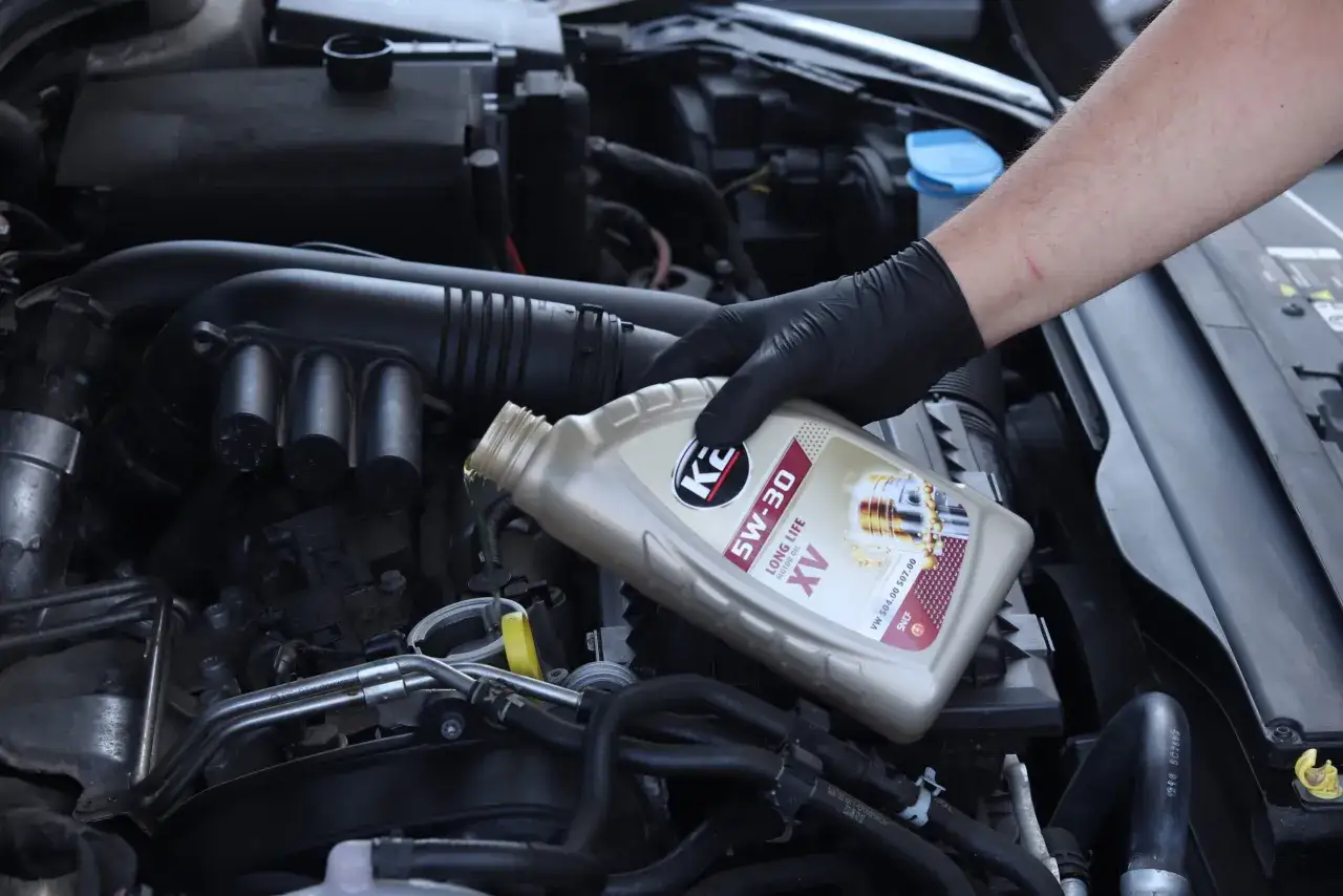 Ręka w czarnej rękawiczce wlewa olej silnikowy 5W-30. Dbałość o żywotność silnika diesel czy benzyna zaczyna się od odpowiedniego smarowania.