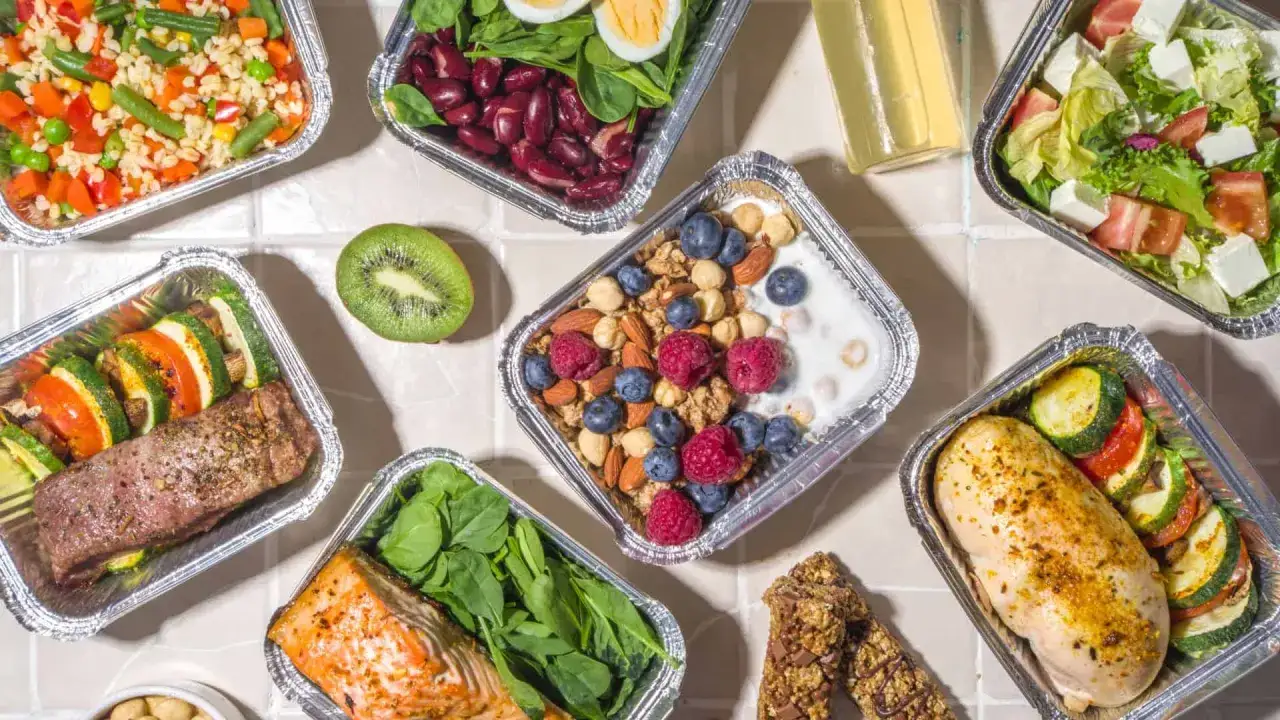 Różnorodne posiłki w pojemnikach: łosoś, kurczak, stek, sałatka, owsianka z owocami. Zastanawiasz się, ile kosztuje catering dietetyczny?