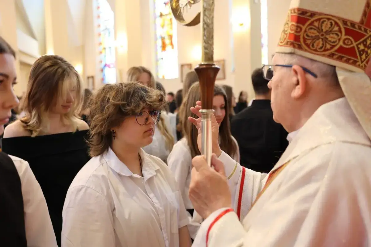 Młoda dziewczyna w okularach przyjmuje sakrament bierzmowania. W jakim wieku to następuje? Zwykle w wieku nastoletnim, jak ona.