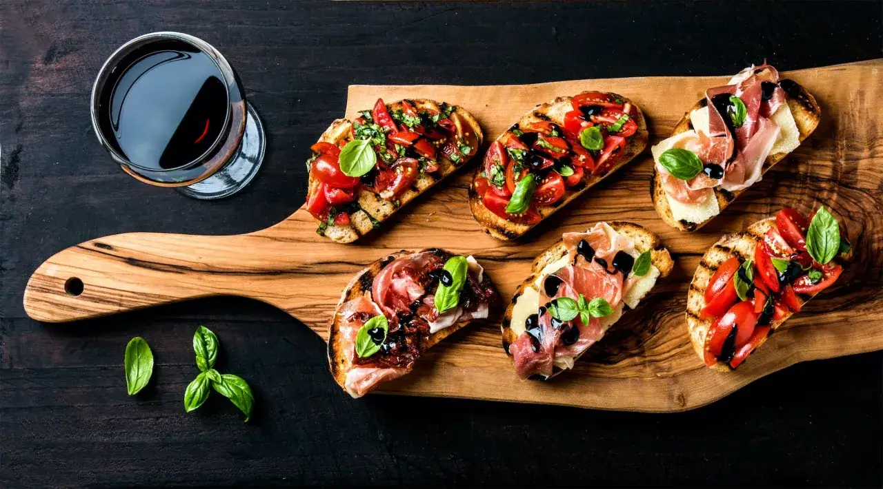 Primitivo kuchnia i wino: bruschetta z pomidorami i szynką parmeńską, ozdobiona bazylią i balsamicznym sosem, obok kieliszek czerwonego wina.