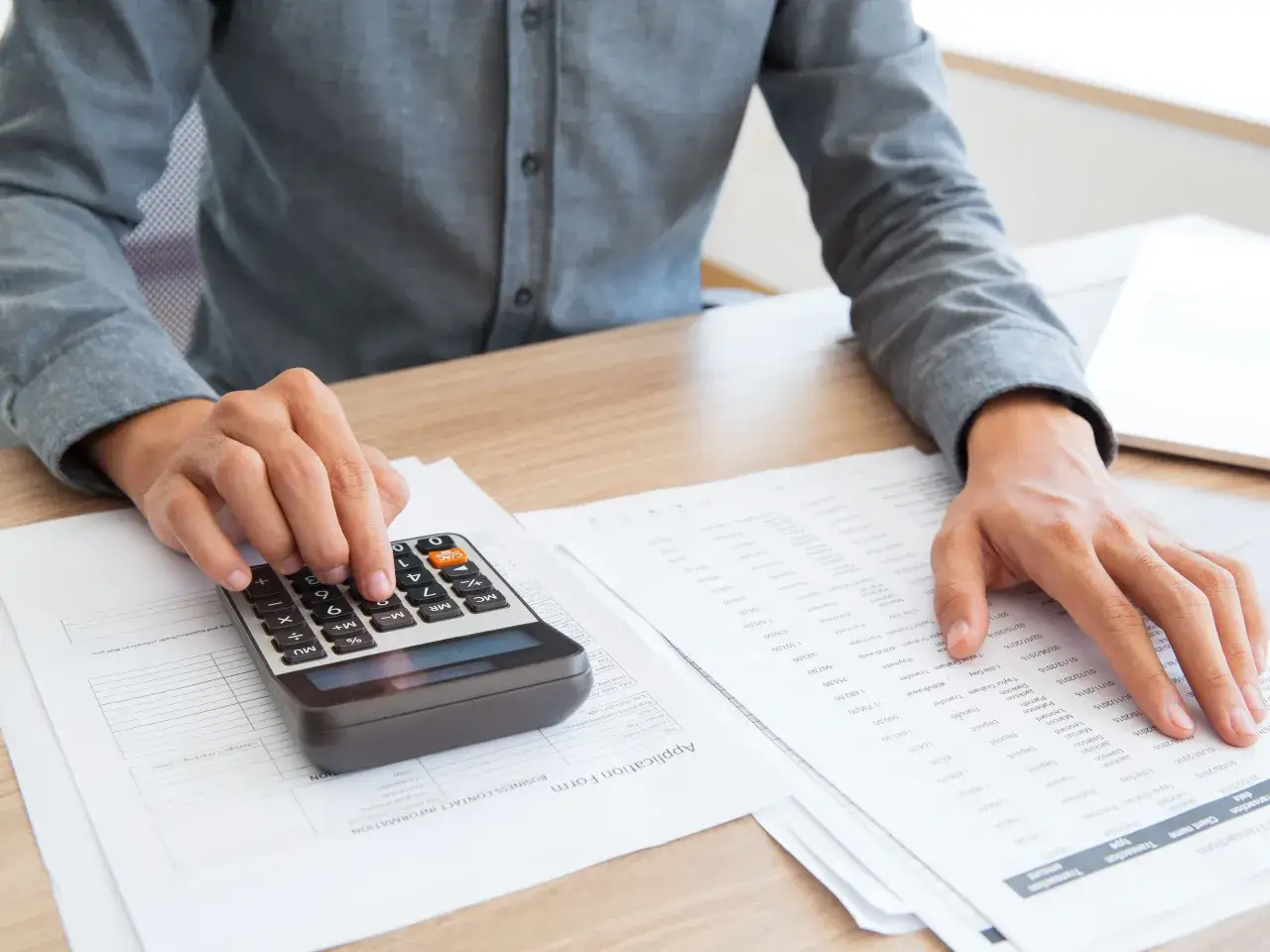 Osoba liczy na kalkulatorze, analizując dokumenty finansowe, by dowiedzieć się, ile można zarobić bez podatku.