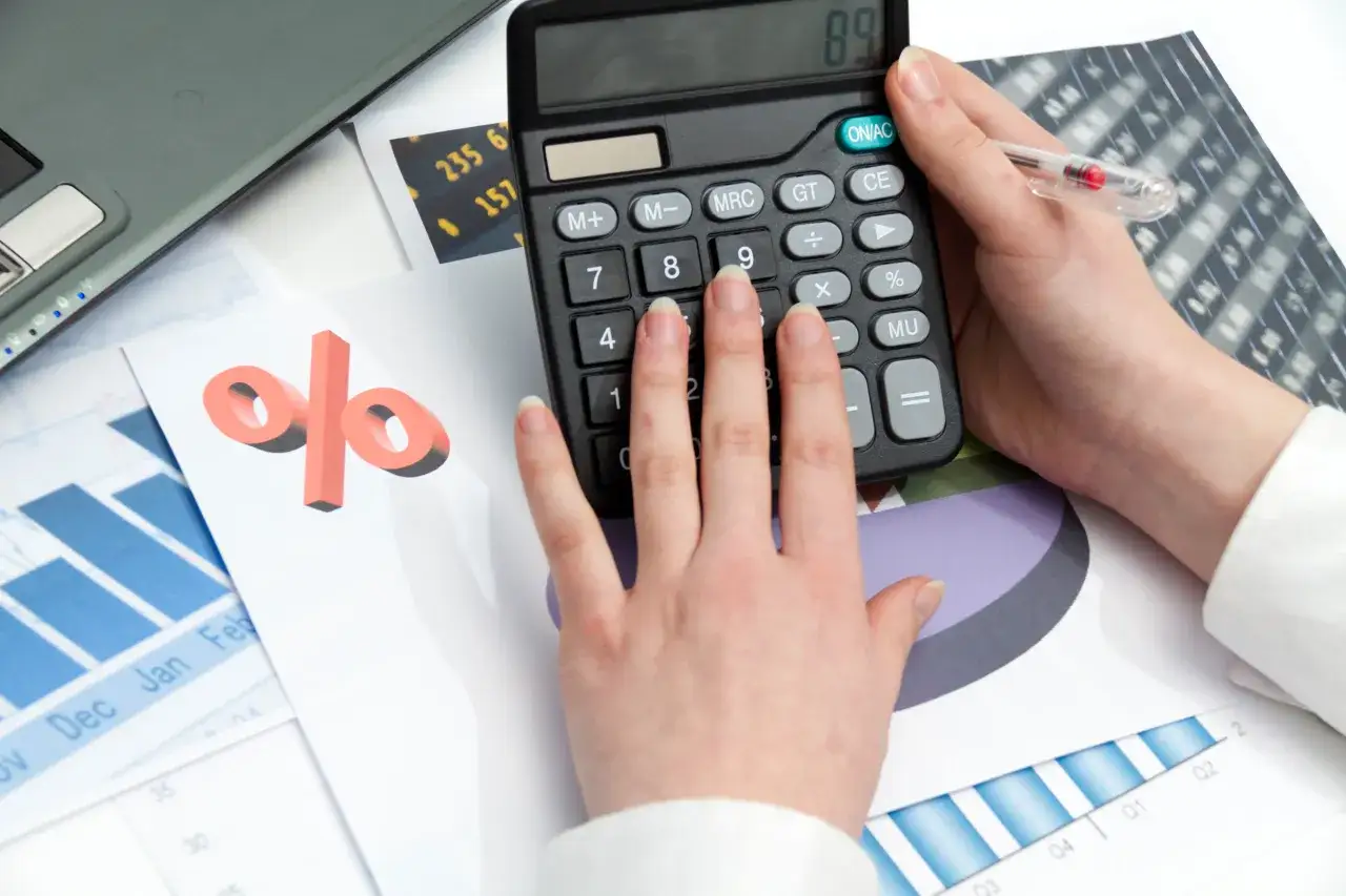 Ręce na kalkulatorze, obok wykres&oacute;w i symbolu procentu. Uczą się, jak obliczyć odsetki od pożyczki.