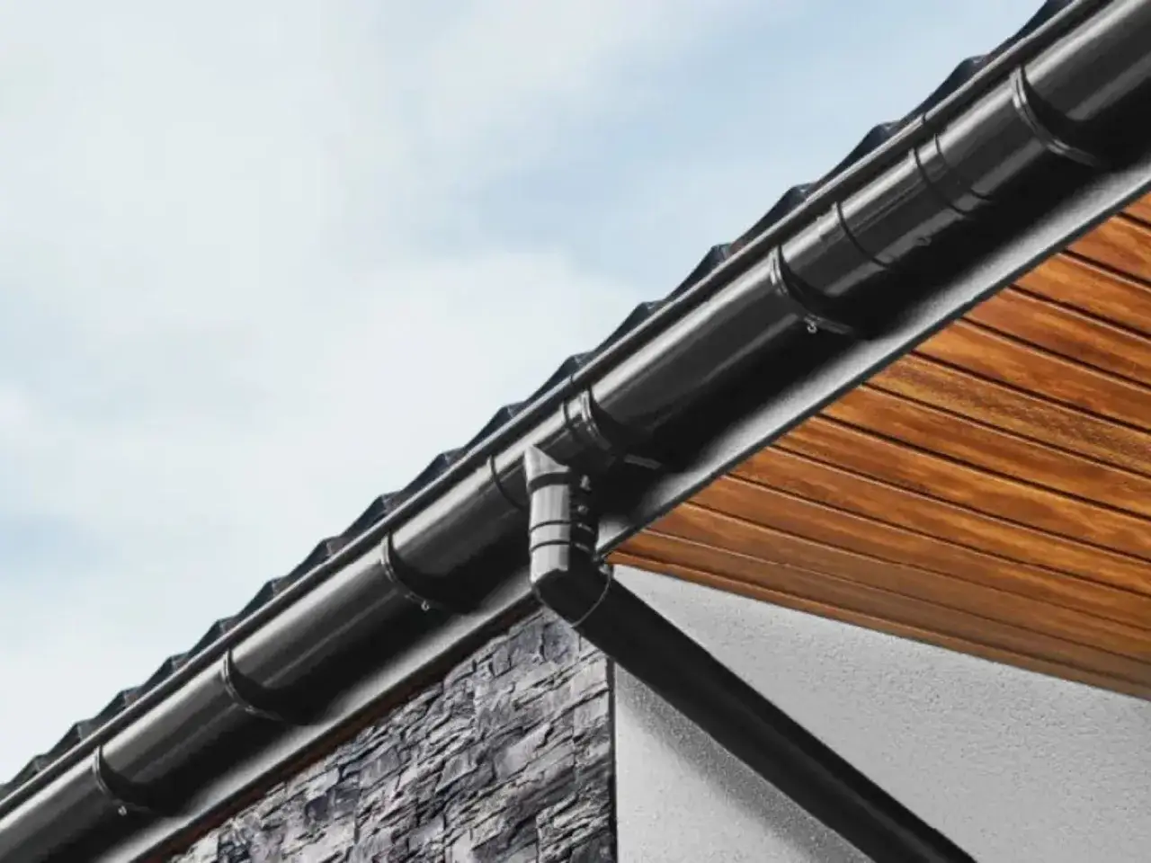 Czarne rury odprowadzające wodę z rynien, zamontowane na dachu z drewnianą podsufitką i kamienną elewacją.
