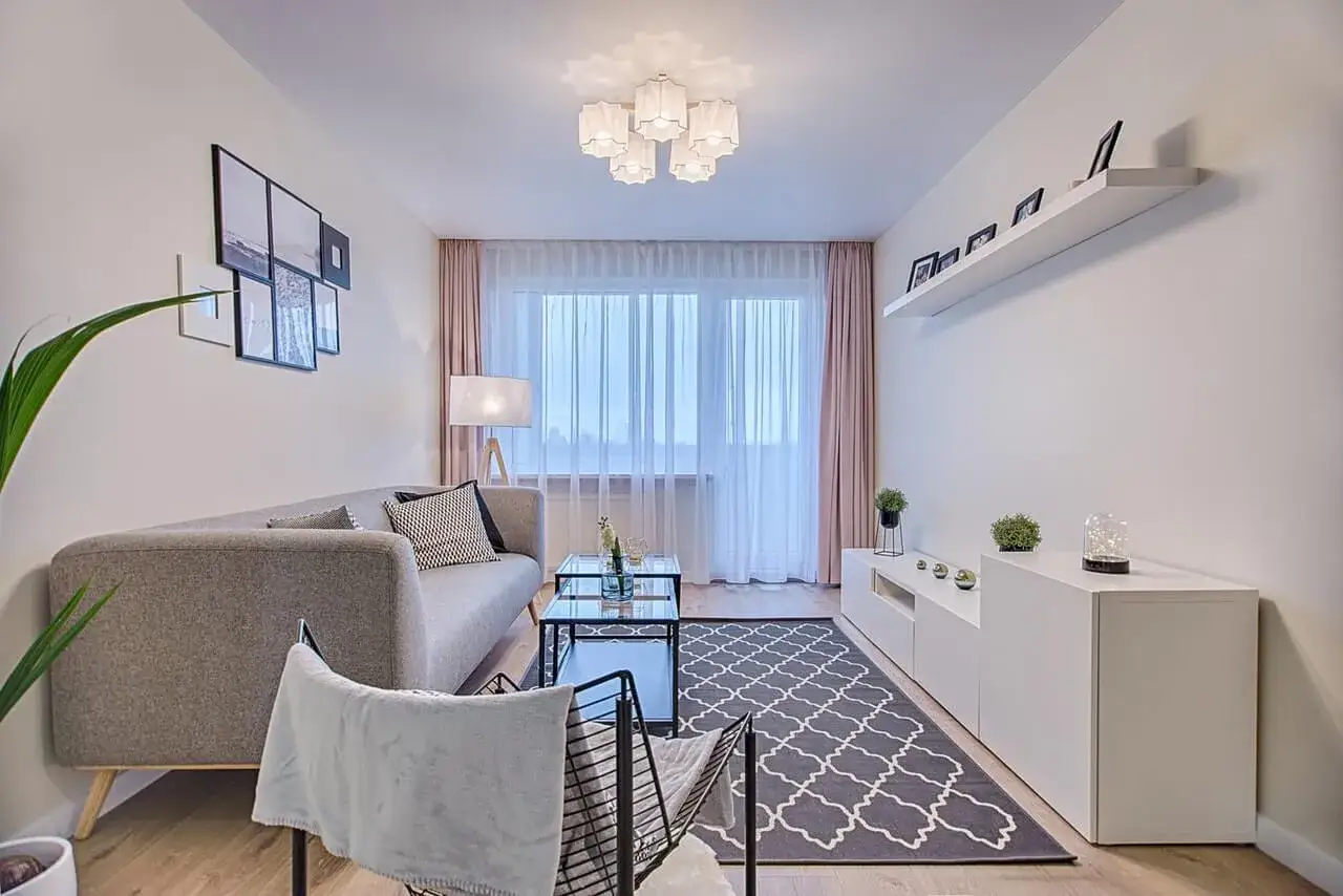 Nowoczesny salon: jak ustawić meble w prostokątnym pokoju. Szara sofa, stolik kawowy, dywan i biała komoda tworzą przytulną przestrzeń.