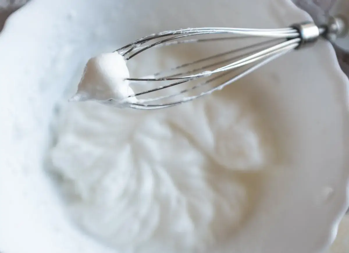 Ubita piana z białek na drucianej trzepaczce w białej misce. Czy białka można mrozić? Tak, można je zamrozić.