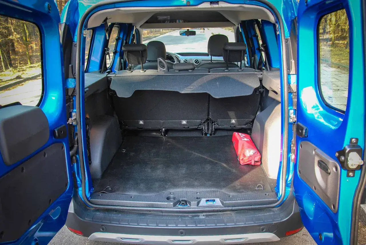 Błękitny Dacia Dokker Stepway z otwartym bagażnikiem. W środku apteczka i widok na tylne siedzenia.