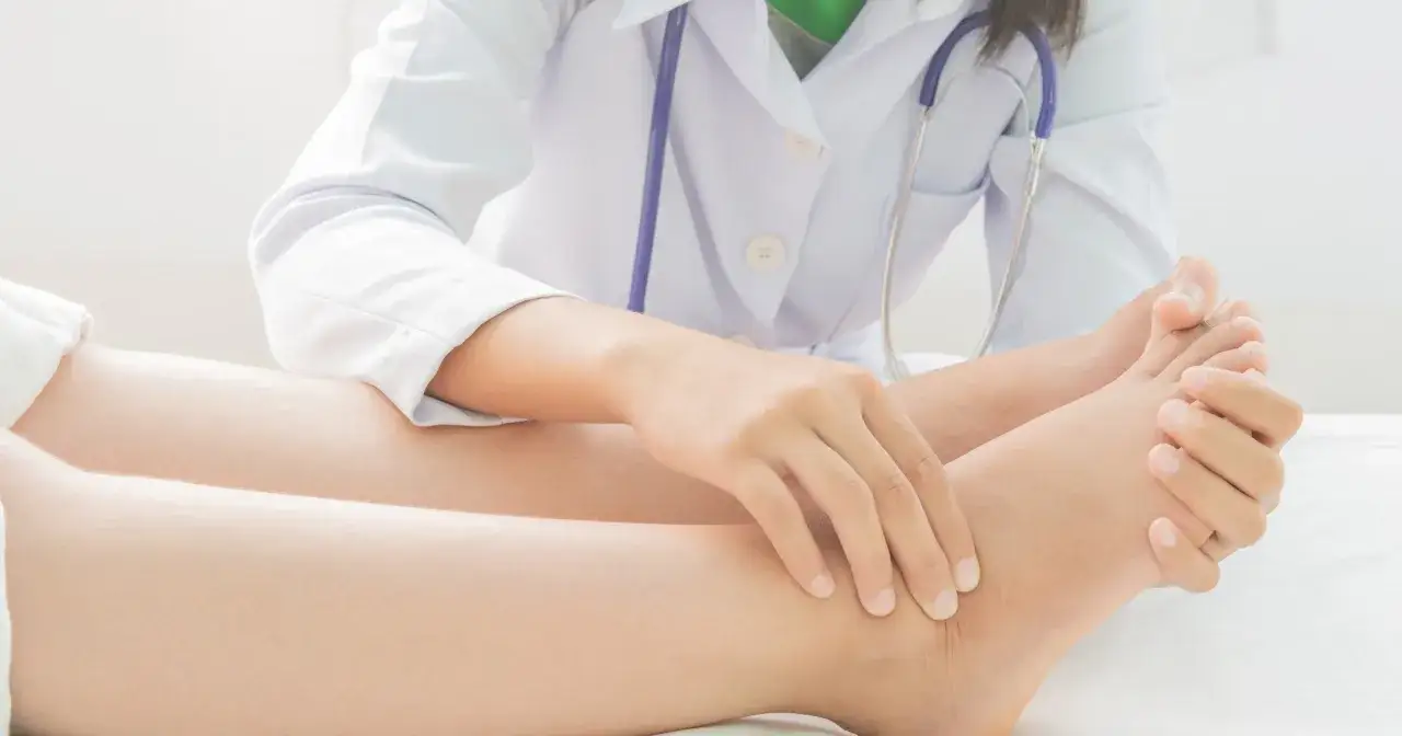 Lekarz bada spuchniętą stopę po porodzie. Dłoń lekarza delikatnie uciska kostkę pacjentki, oceniając obrzęk.