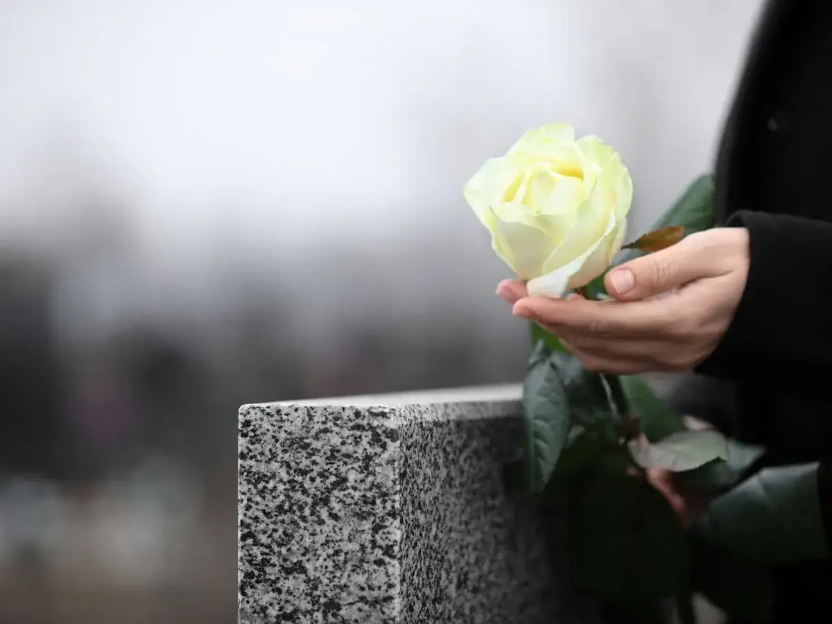 Dłoń trzyma białą różę przy nagrobku. Pytanie, jak długo nie można ruszać rzeczy zmarłego, wciąż pozostaje.
