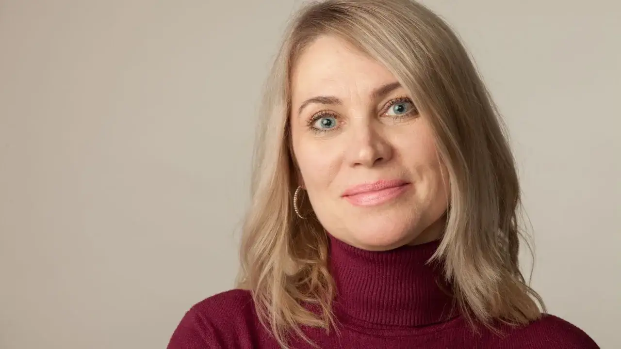 Blondynka po 50. z niebieskimi oczami i delikatnym uśmiechem, zastanawia się, jakie zabiegi na twarz po 50. będą najlepsze.