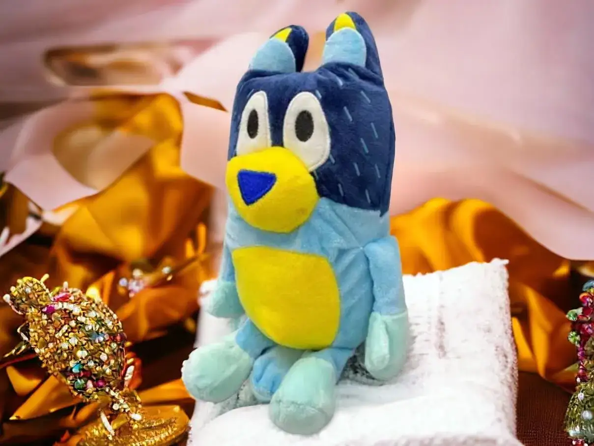 Urocza maskotka dla niemowlaka, niebieski piesek Bluey, siedzi na białym ręczniku.