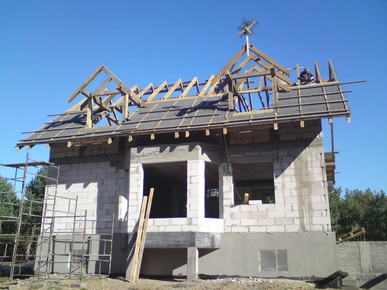 Dom w budowie, na szczycie dachu widoczna drewniana wiecha na dach.