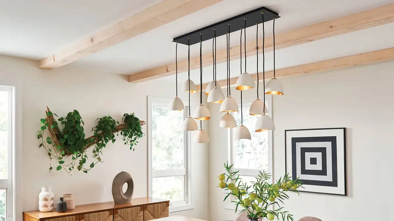 Nowoczesny system oświetlenia szynowego z wieloma białymi kloszami, tworzący elegancki żyrandol nad stołem.