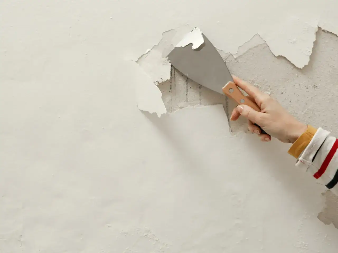 Dłoń z kielnią usuwa łuszczącą się warstwę starego tynku. Prosty spos&oacute;b, jak szybko usunąć stary tynk.