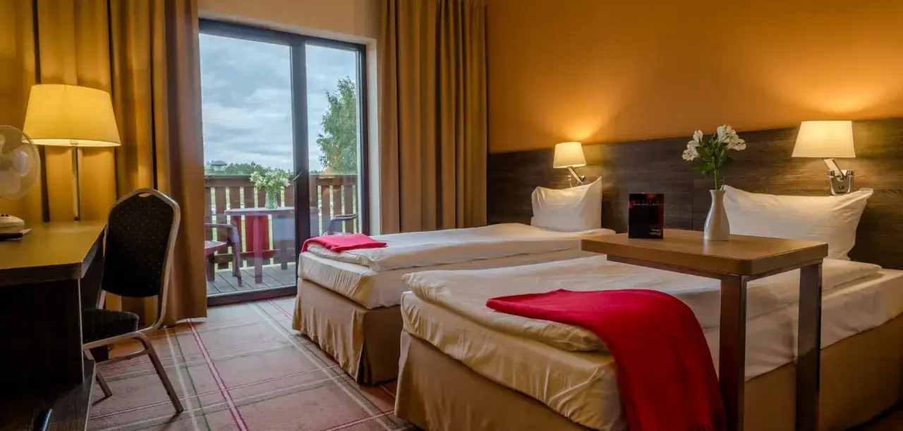 Pok&oacute;j hotelowy z dwoma ł&oacute;żkami, balkonem i widokiem na zieleń. Idealne miejsce na **weekend z rodziną**.