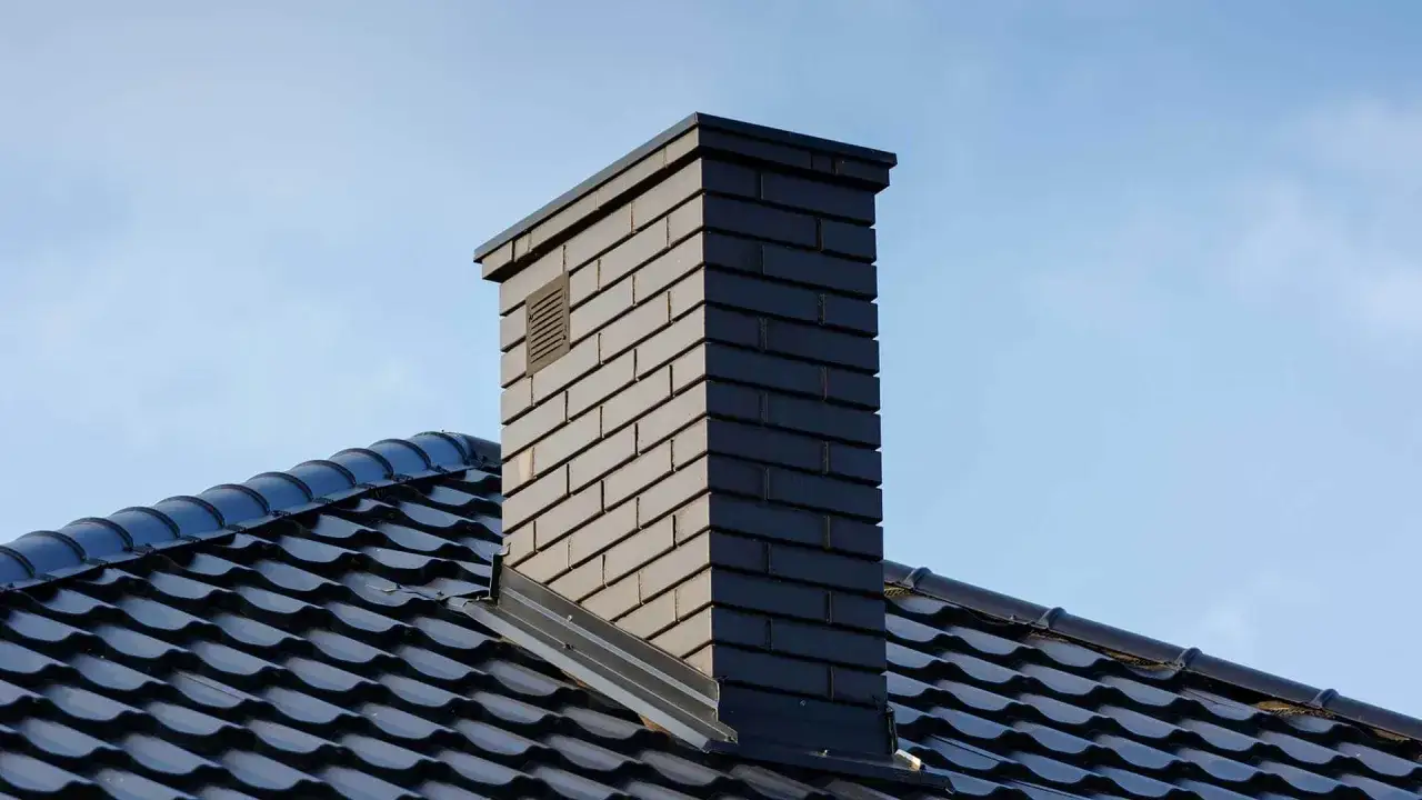Nowy, ciemny komin z cegły na czarnym dachu. Zastanawiasz się, ile kosztuje wymurowanie komina?