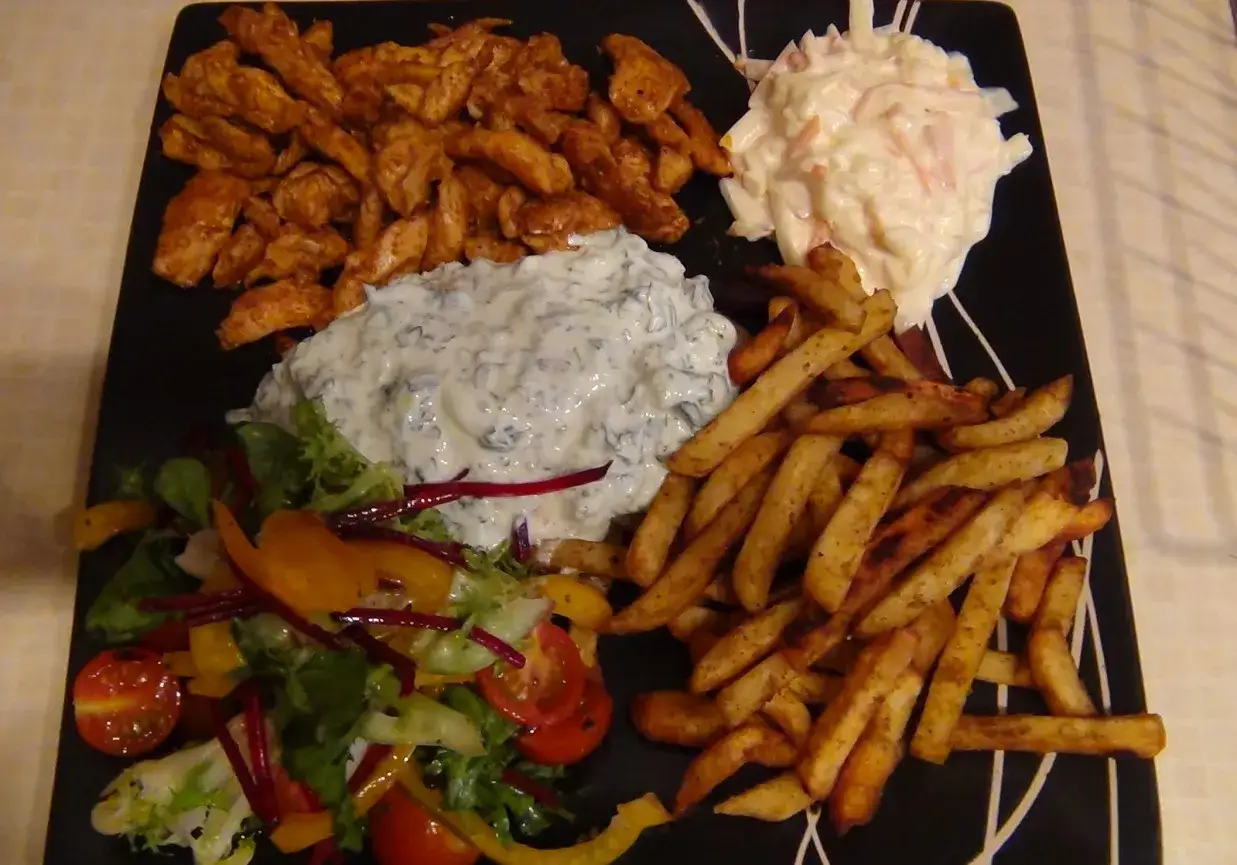 Pyszna shoarma z kurczaka z frytkami, sałatką i sosem czosnkowym na czarnym talerzu.