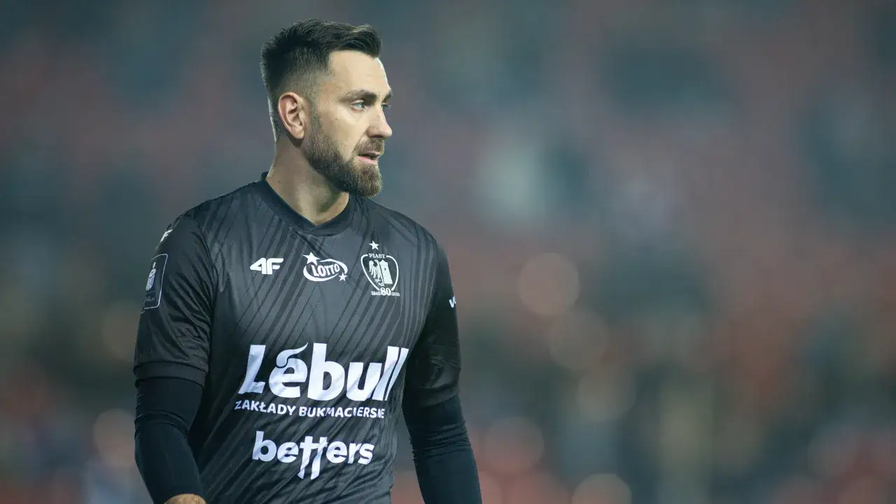 Bramkarz Piasta Gliwice w czarnej koszulce z logo klubu i sponsorami. Jeden z zawodników Piasta Gliwice gotowy do gry.