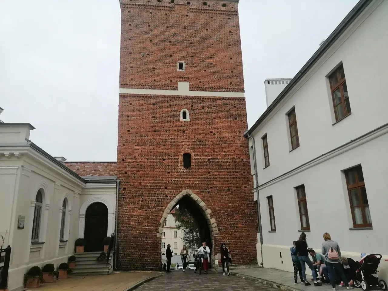 Brama w Sandomierzu, jedna z atrakcji miasta. Ludzie spacerują pod ceglaną wieżą, zwiedzając sandomierz i okolice atrakcje.