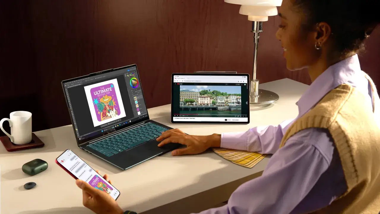 Kobieta pracuje przy laptopie, na którym widać program graficzny. Obok tablet z filmem na YouTube. Telefon pokazuje powiadomienia, co może pomóc w ustaleniu, jak sprawdzić jakie aplikacje były uruchamiane.